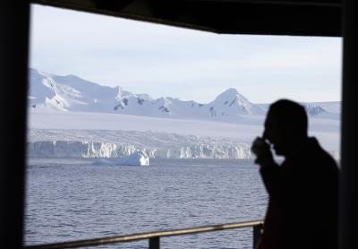 un hombre bebiendo una taza de café en la cubierta de un barco frente a la Península Antártica, a la altura de las Islas Shetland del Sur.