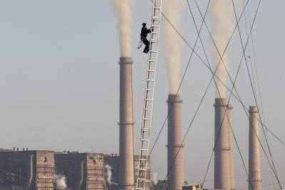 Un trabajador se encarama en una escalera entre las chimeneas de una fábrica.