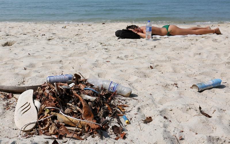 Un mujer toma el sol en una playa del parque Nacional de Penang (Malasia) junto un montón de basura recogida del mar.
