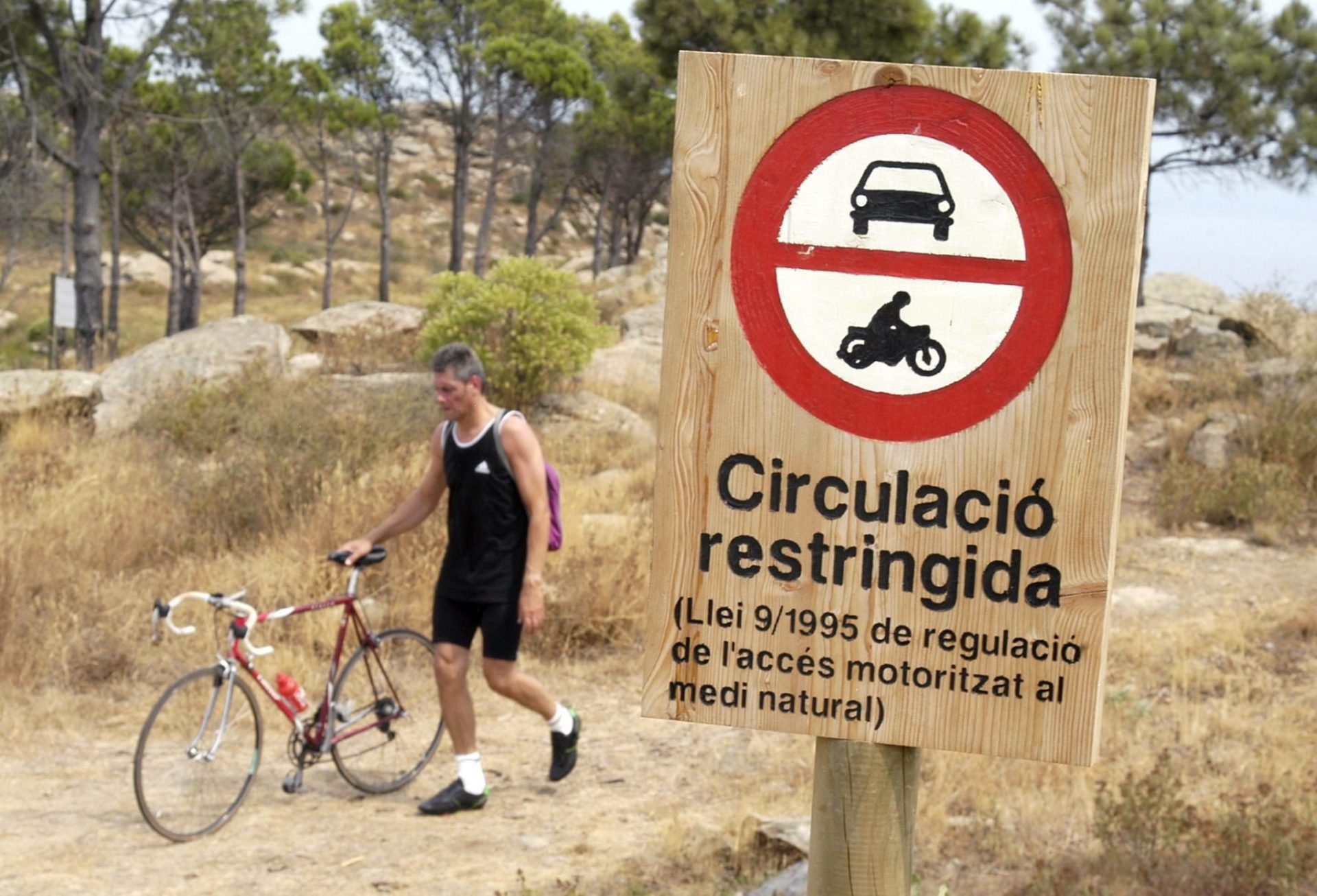 Un ciclista pasa por un cartel que protege un área natural.