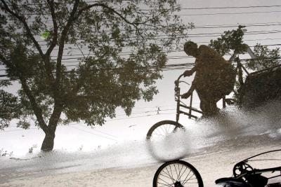 Un ciclista pedalea bajo la lluvia mientras su imagen se refleja en un charco en Pekín (China)
