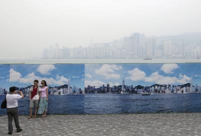 Dos turistas se toman fotos ante un póster que muestra un paisaje de Hong Kong un día despejado, mientras, detrás se ve la ciudad cubierta de una niebla a causa de la contaminación.