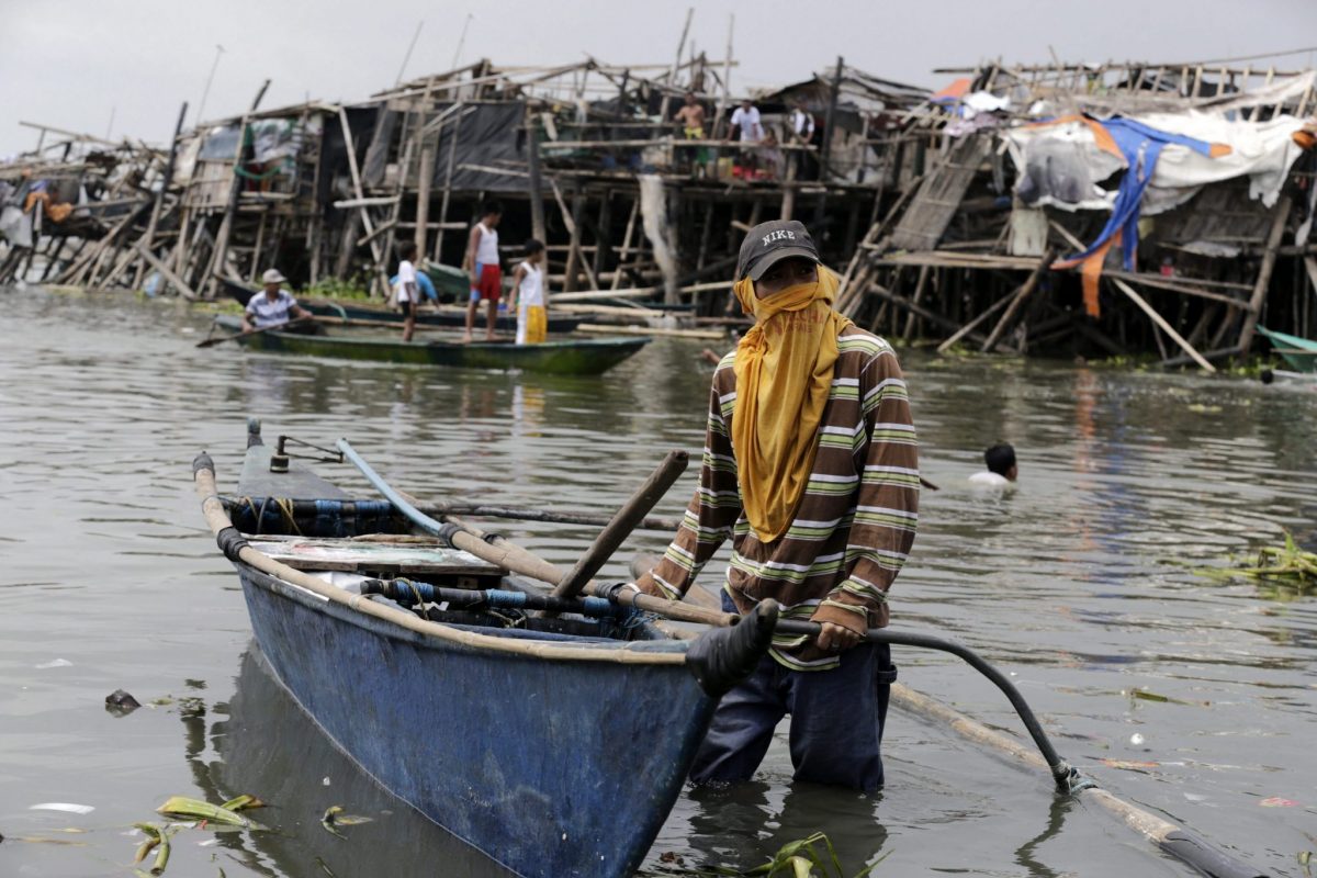 Un filipino empuja una barca entre casas destruidas por el tifón Rammasun.