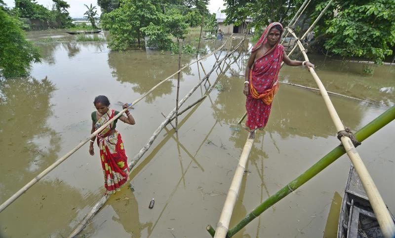 Dos mujeres indias atraviesa una zona inundada a través de unos troncos de bambú