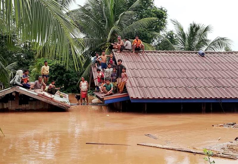 Un grupo de personas aguarda en lo alto de un tejado en una zona inundada
