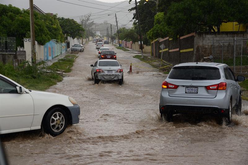 Vehículos transitan por una vía inundada debido a fuertes lluvias por el paso del huracán Matthew en Kingston (Jamaica).  