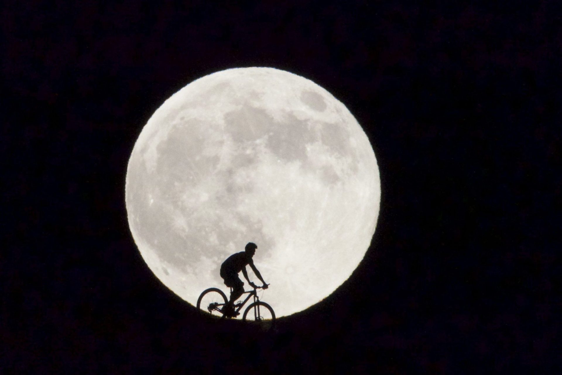 Un ciclista pasa delante de la Luna llena que se observa hoy en la isla canaria de Fuerteventura .
