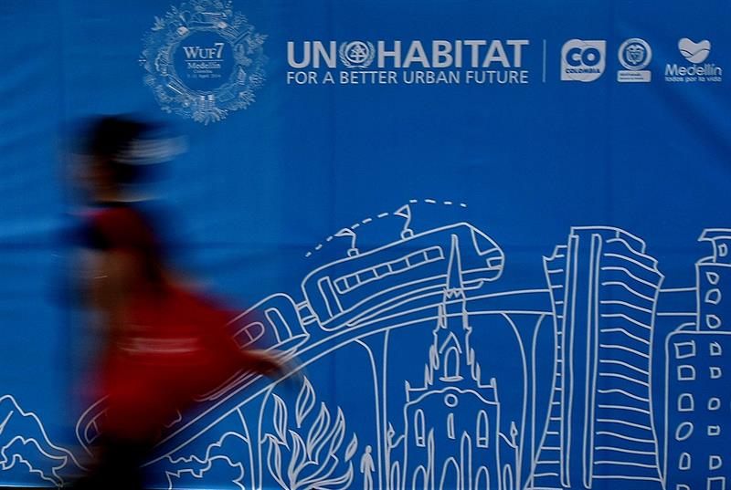 Una mujer camina frente a un cartel del VII Foro Urbano Mundial,