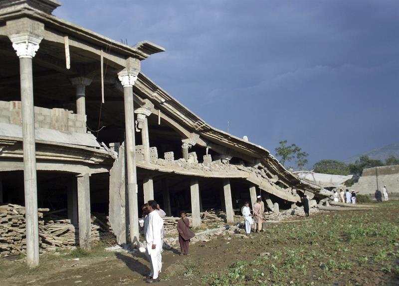 Varios hombres observan un edificio destruido por el terremoto  en Buner, Pakistán.