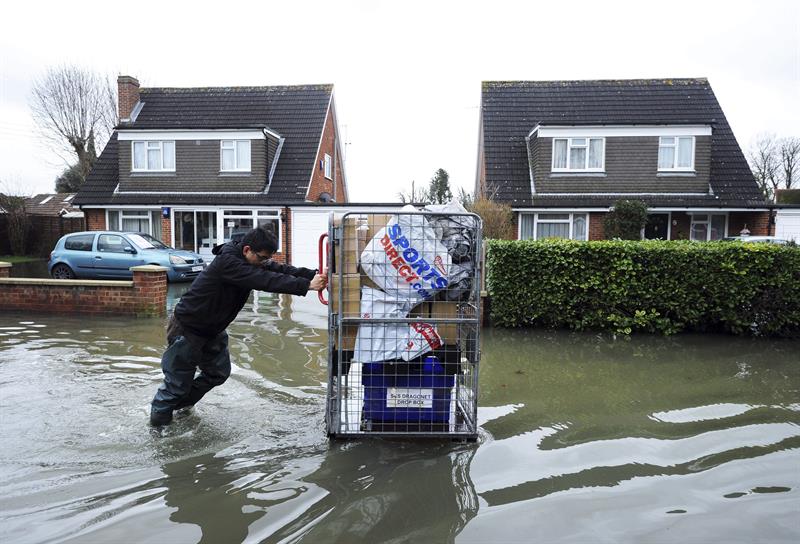 Un hombre empuja un carro con sus pertenencias a través de una calle inundada de Surrey, cerca de Londres (Reino Unido)