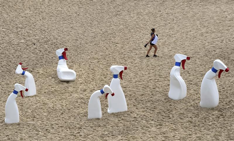 Una joven pasa junto al conjunto de esculturas titulado "Las Botellas", del colectivo de artistas RCM, que se exhiben dentro de la exposición anual al aire libre "Esculturas junto al Mar". 