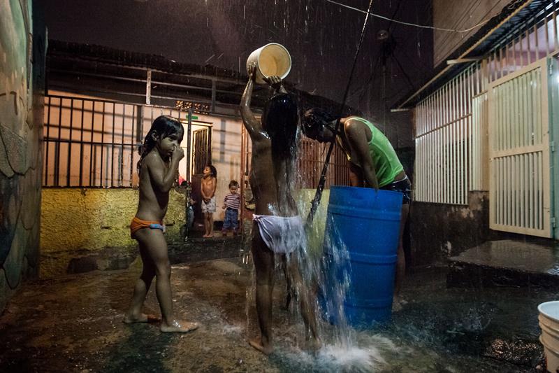 Niños y adultos del barrio de La Bombilla, en Caracas, se duchan en la calle con el agua de lluvia recogida. 
