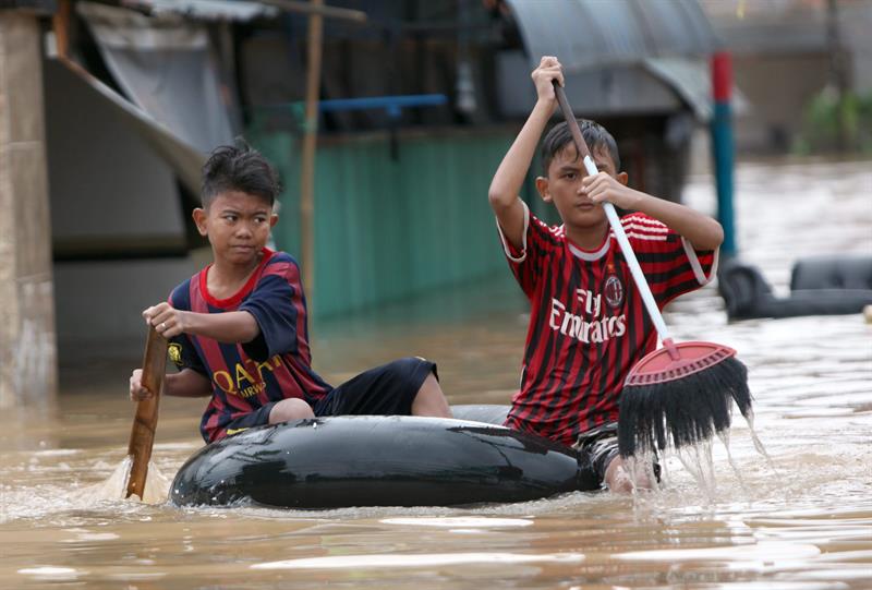 Dos chicos indonesios se escapan en un bote improvisado y ayudados con escobas de las inundaciones que ya han provocado al menos 10 muertos y más de 60.000 evacuados.