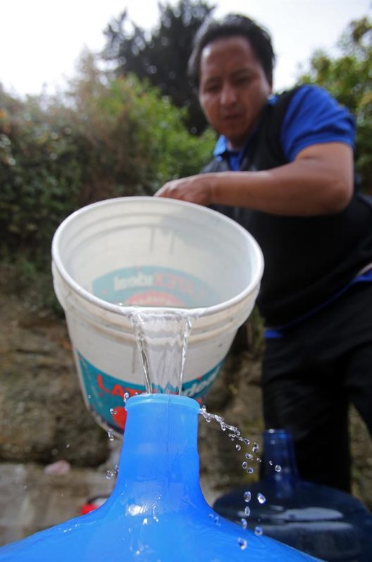 Abastecimiento de agua en cubos y botellas en una ladera de La Paz, donde 94 barrios sufren cortes de agua debido a la sequía.