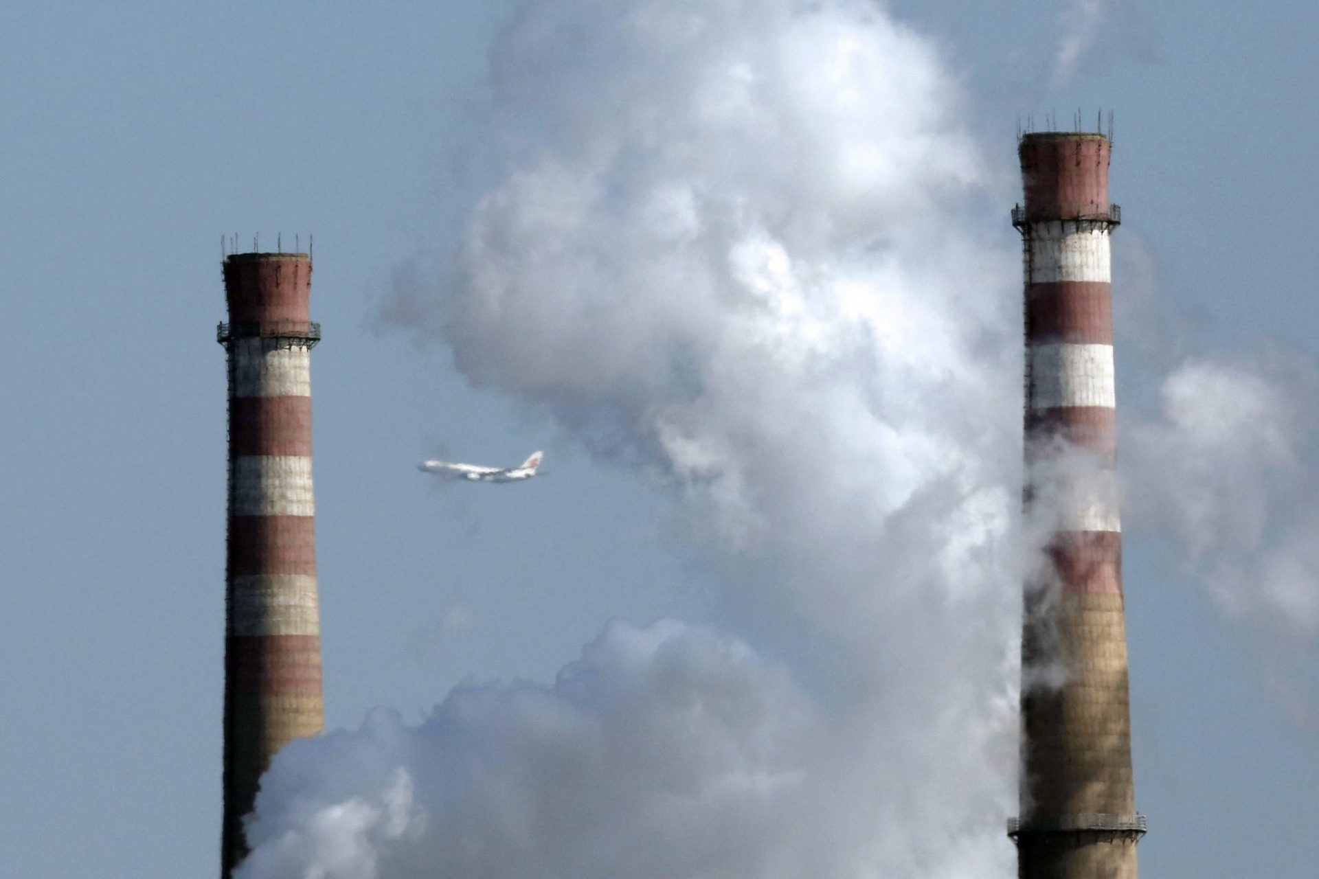 Un avión vuela entre dos torres de refrigeración y una columna de humo en Pekín.