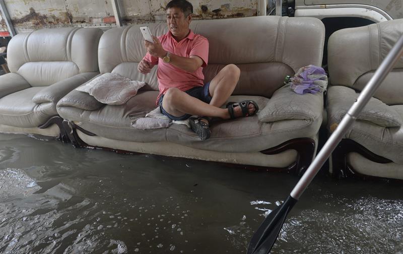 un hombre sentado en un sofá mientras toma fotos de las inundaciones, en Shenyang, provincia de Liaoning, al nordeste de China. 