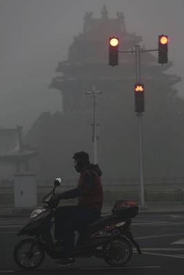 Un hombre circula en moto por las calles de Pekín (China), donde apenas se ven los edificios por la nube de contaminación del aire. 