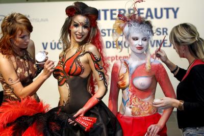 Dos artistas del maquillaje pintan a sendas modelos en una feria internacional de cosméticos