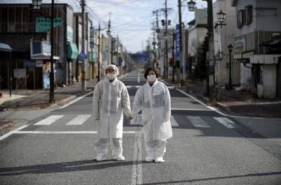 La pareja formada por Yuzo Mihara (izda) y su mujer, Yuko, vestidos con trajes y máscaras protectoras, posan para el fotógrafo en una calle desierta de la abandonada localidad de Namie (Fukushima) en 2013, dos años después de tener que evacuarlo por el desastre nuclear.