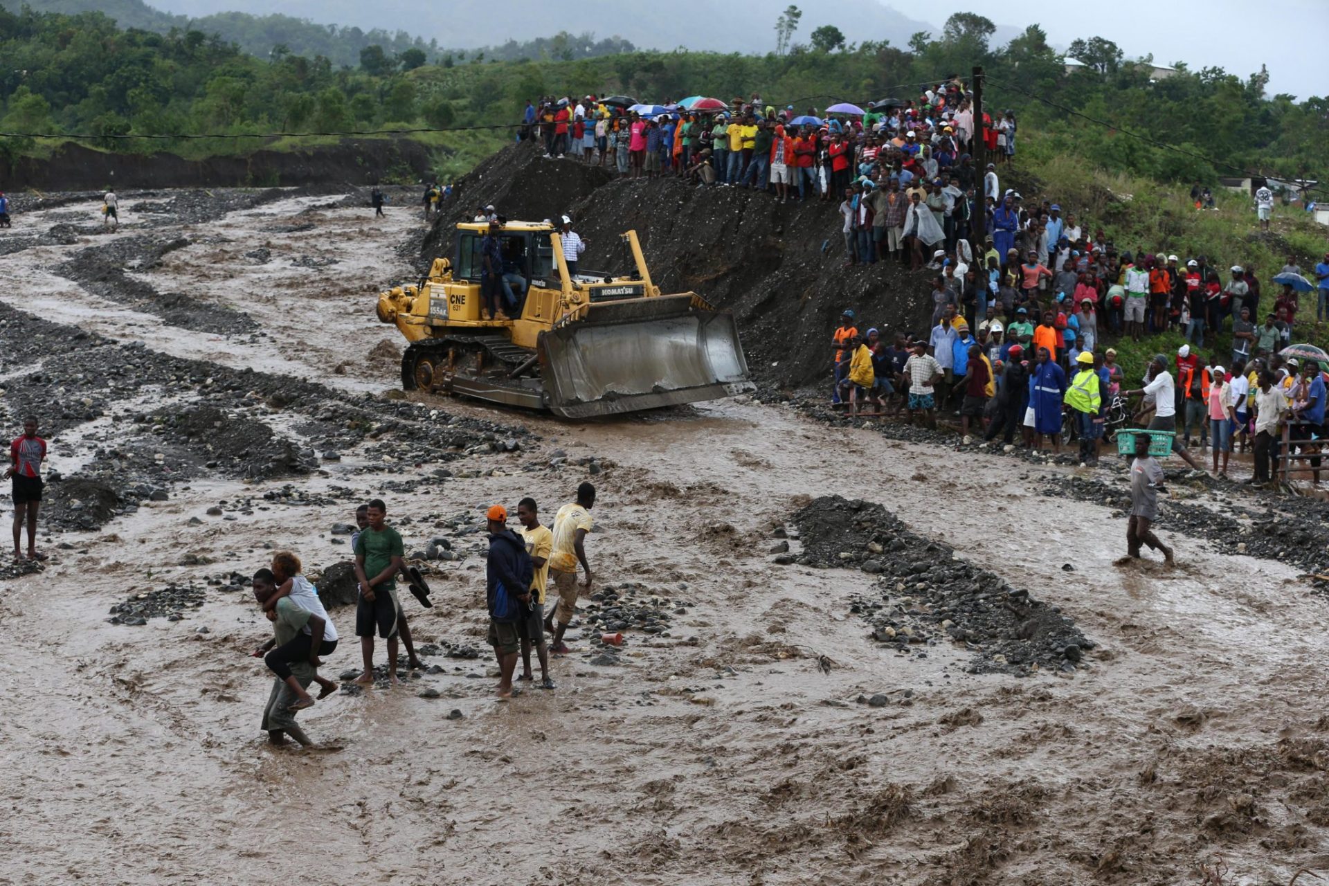 Haitianos a la espera de cruzar a pie un río cuyo único puente destrozó el huracán Matthew