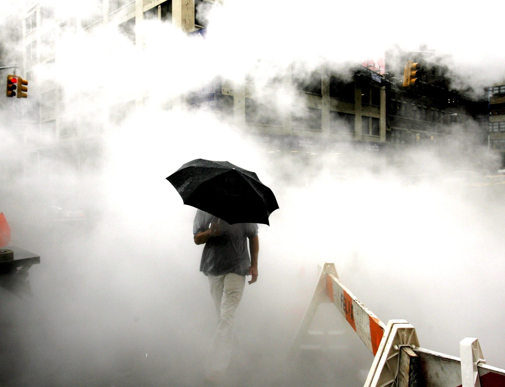 Un hombre con un paraguas atraviesa el vapor que sube del asfalto.
