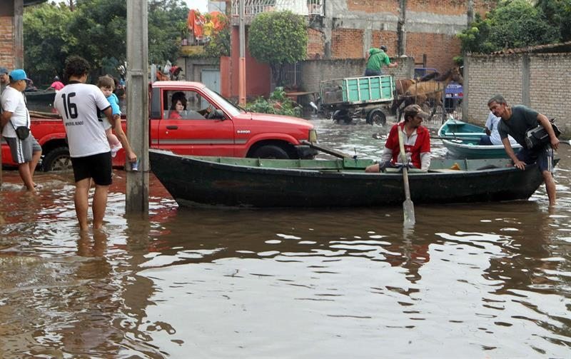 Un coche y una barca comparten una calle inundada de un barrio de Asunción (Paraguay)