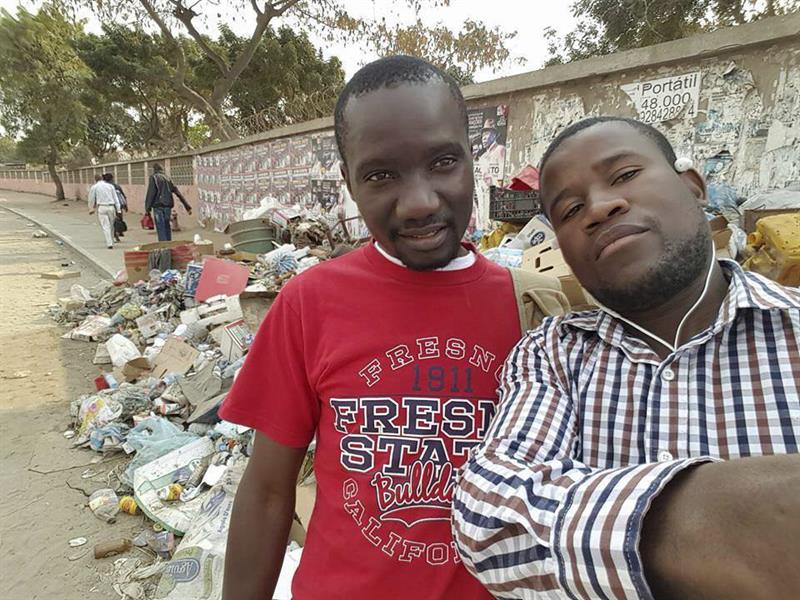 Dos jóvenes posan delante de un montón de basura acumulada en una calle de Luanda. EFE/Selfie-Lixo 