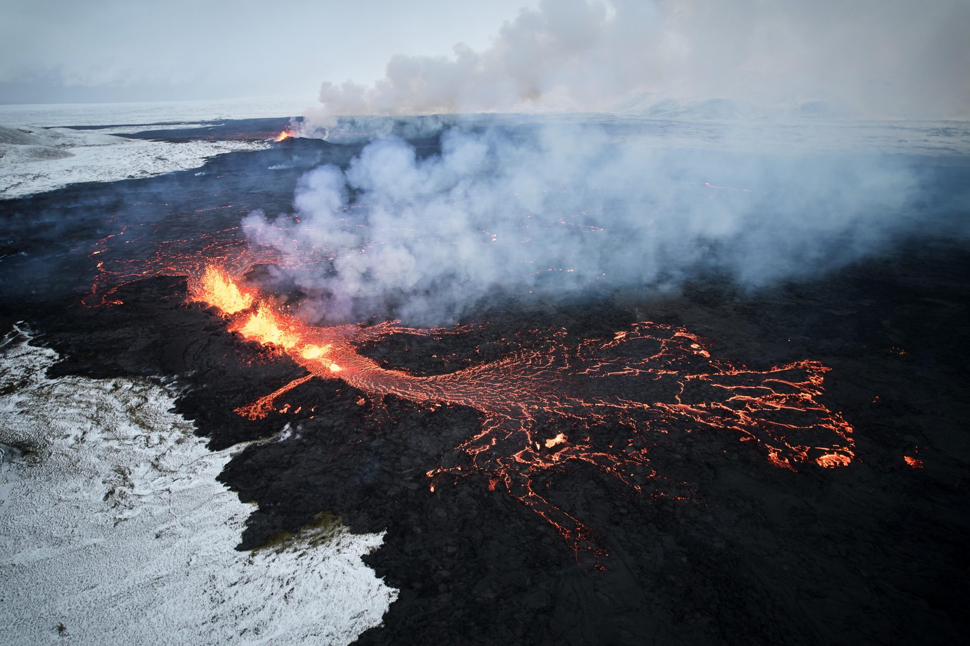 Fotografía aérea tomada con un drone muestra lava y humo saliendo de una fisura volcánica durante una erupción cerca de la ciudad de Grindavik, en la península de Reykjanes (Islandia). La Oficina Meteorológica de Islandia (OMI) anunció el inicio de una erupción volcánica fisural cerca del cráter de Sundhnuka, al noreste de Grindavik, en la noche del 18 de diciembre, tras semanas de intensa actividad sísmica en la zona. La potencia y la actividad sísmica de la erupción han disminuido con el tiempo, informó la OMI el 19 de diciembre, añadiendo que se han registrado unos 320 seísmos desde el inicio de la erupción. EFE/EPA/ANTON BRINK