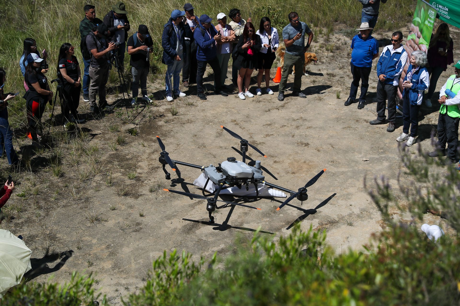 Personas observan al dron forestal Agras T20, de tecnología china, lanzando 20.000 semillas de especies nativas que apuntan a recuperar la cobertura vegetal del árido y erosionado cerro Casitagua, afectado en parte por un incendio el año pasado, el 02 de mayo de 2024 en Quito (Ecuador). EFE/José Jácome