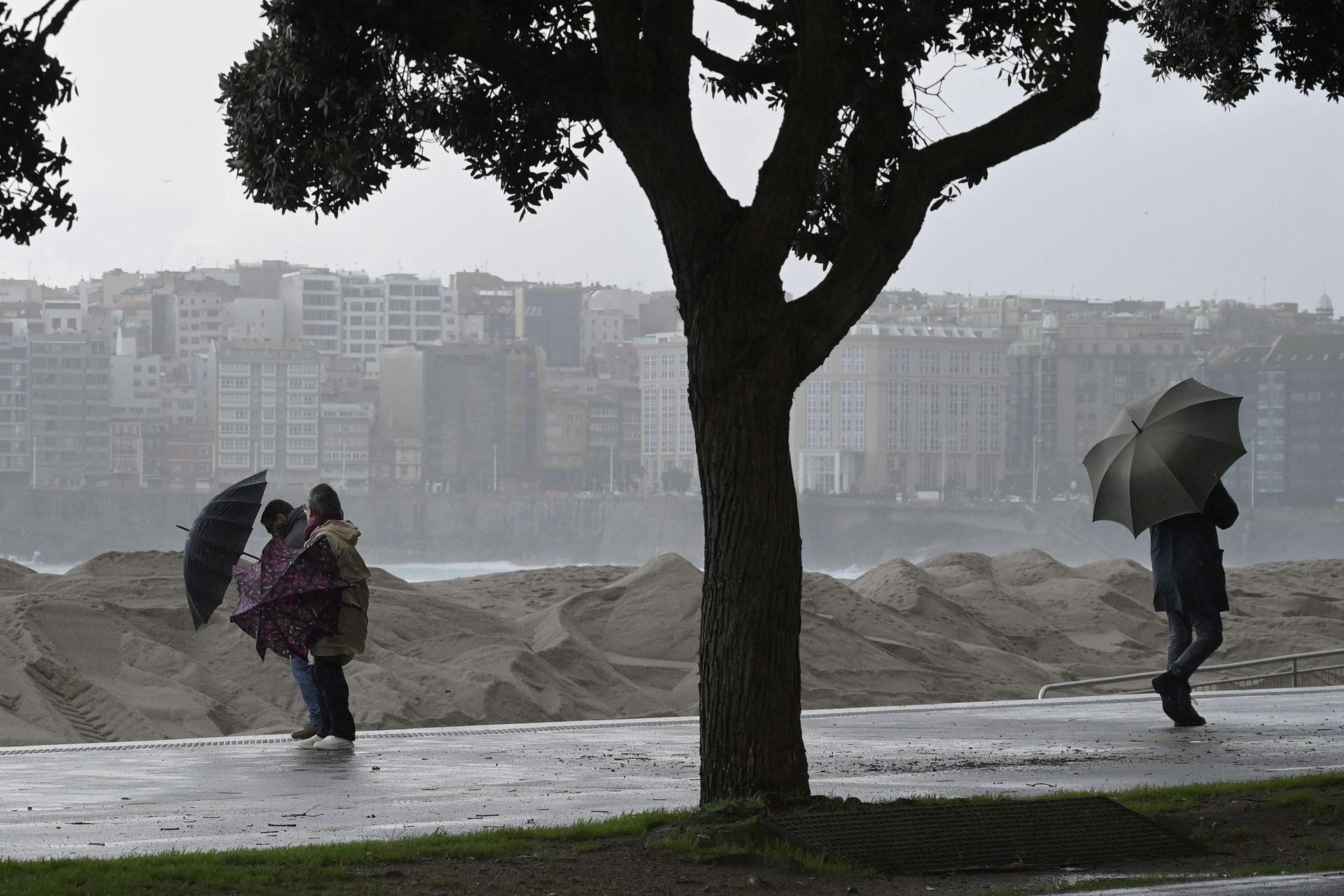 A CORUÑA, 21/01/2026.- Varias personas se protegen de la lluvia junto a la costa de A Coruña este miércoles. El litoral coruñés está este miércoles en alerta roja con lluvias intensas, viento fuerte y suspensión de toda la actividad deportiva en el mar. EFE / Moncho Fuentes