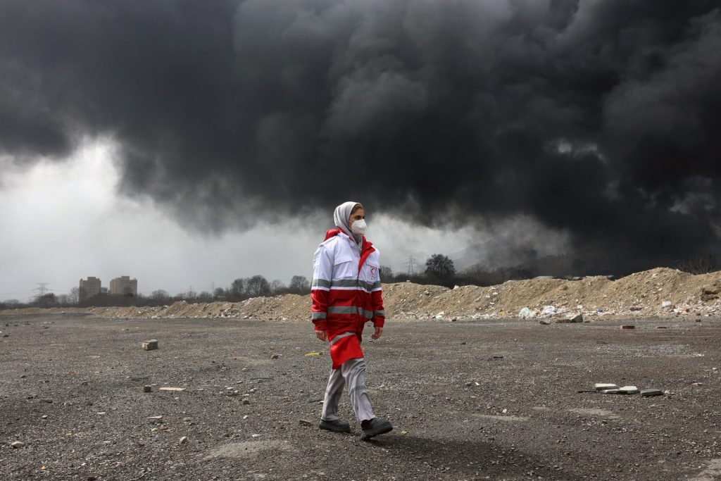 TEHRAN (IRAN (Islamic Republic Of)), 08/03/2026.- A member of Iran's Red Crescent walks as smoke still rises from Shahran Oil Refinery following last night airstrike in Tehran, Iran, 08 March 2026. A joint Israeli and US military operation continues to target multiple locations across Iran since the early hours of 28 February 2026. (Teherán) EFE/EPA/ABEDIN TAHERKENAREH