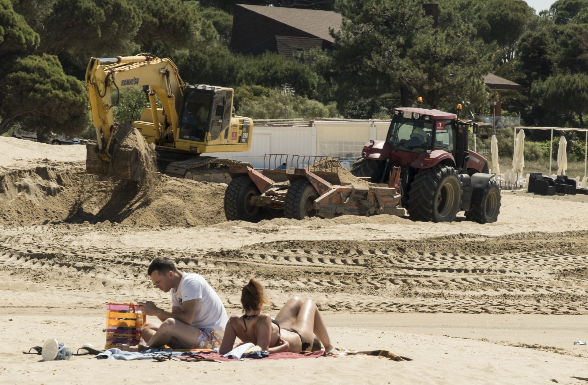 ANDALUCÍA. HU02. CARTAYA (HUELVA), 28/05/2018 - Una pareja toma el sol en la playa del Nuevo Portil, en Cartaya (Huelva) mientras las máquinas trabajan en las obras de regeneración de las playas onubenses afectadas por los temporales del pasado invierno para las que se precisará un volumen de arena de 900.000 metros cúbicos, EFE/Julián Pérez